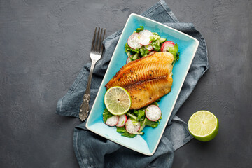 Grilled fish sea bass with fresh herbs, radish and lime in a rectangular blue plate. Dark...