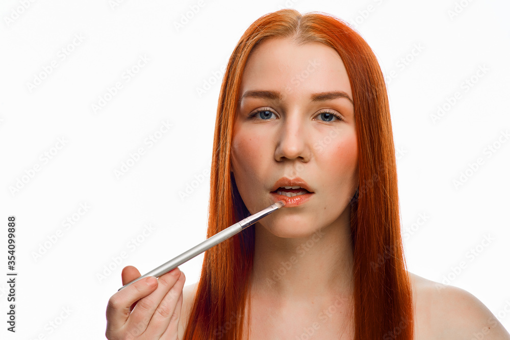 Wall mural close beauty portrait of a red-haired girl with a brush for applying makeup. isolated on a white bac