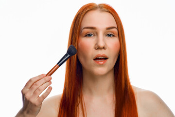 Obraz premium close beauty portrait of a red-haired girl with a brush for applying makeup. Isolated on a white background.