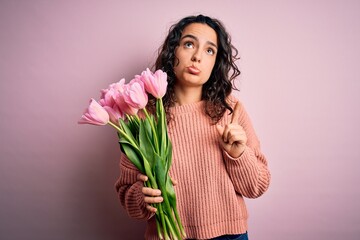 Young beautiful romantic woman with curly hair holding bouquet of pink tulips Pointing up looking sad and upset, indicating direction with fingers, unhappy and depressed.