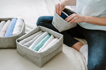 Woman folding clothes, organizing stuff in boxes and baskets. Concept of minimalism lifestyle and...