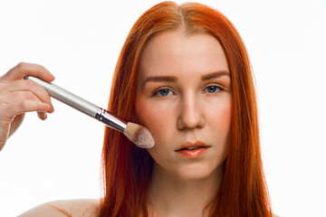 close beauty portrait of a red-haired girl with a brush for applying makeup. Isolated on a white background.