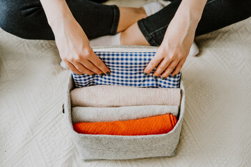 Woman folding clothes and organizing stuff in boxes and baskets. Concept of minimalism lifestyle...