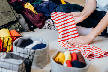 Woman folding clothes on the floor, organizing stuff in baskets and boxes. Concept of clothes...