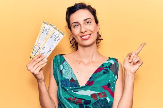 Young beautiful hispanic woman holding boarding pass smiling happy pointing with hand and finger to the side