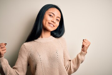 Young beautiful chinese woman wearing casual sweater over isolated white background very happy and excited doing winner gesture with arms raised, smiling and screaming for success. Celebration