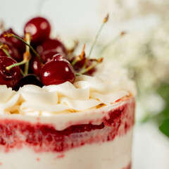 Red berry cake decorated with cherry berries and white cream, among lilac flowers and green leaves. Food photography. Advertising and commercial design.