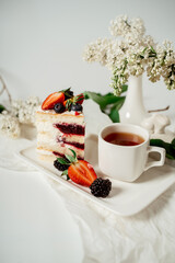 Sliced white berry cream cake decorated with strawberries and blackberries, among lilac flowers and green leaves. Food photography. Advertising and commercial close up design.