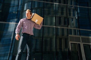 Portrait of a young male businessman who is holding a paper box for moving to another office.