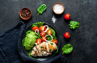 
Grilled chicken breast and avocado salad with cherry tomatoes, spinach, in a black plate on a stone  background 
with copy space for your text