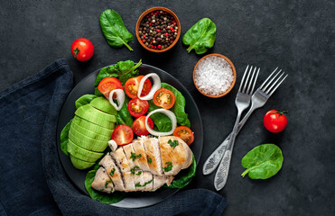 
Grilled chicken breast and avocado salad with cherry tomatoes, spinach, in a black plate on a stone background