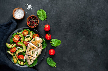 
Grilled chicken breast and grilled avocado salad with cherry tomatoes, spinach, in a black plate...
