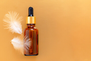Oil bottle with pipette on the golden background with white feathers and copy space. Skin care concept