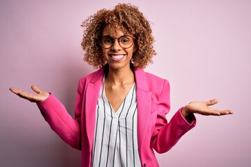 Young african american businesswoman wearing glasses standing over pink background smiling showing both hands open palms, presenting and advertising comparison and balance