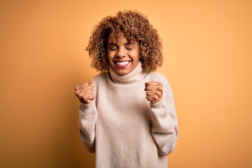 Young beautiful african american woman wearing turtleneck sweater over yellow background excited...