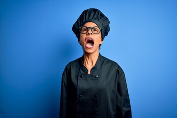 Young african american chef woman wearing cooker uniform and hat over blue background angry and mad screaming frustrated and furious, shouting with anger. Rage and aggressive concept.