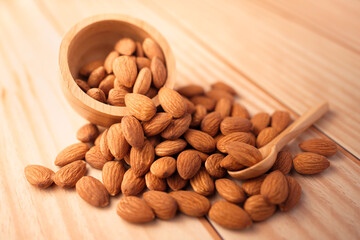 organic peeled brown almonds pour from wooden bowl and spoon on wood table. concept of vegan raw ingredient for vegetarian, snack and healthy food.
