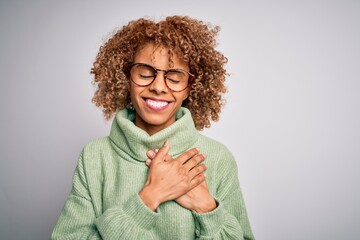 Young beautiful african american woman wearing turtleneck sweater and glasses smiling with hands on chest with closed eyes and grateful gesture on face. Health concept.