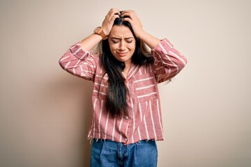 Young brunette woman wearing casual striped shirt over isolated background suffering from headache desperate and stressed because pain and migraine. Hands on head.