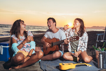 Group of friends with guitar having fun on the beach at sunset.