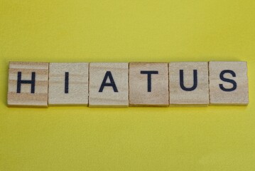  the gray word hiatus of gray small wooden letters lie on a yellow  table