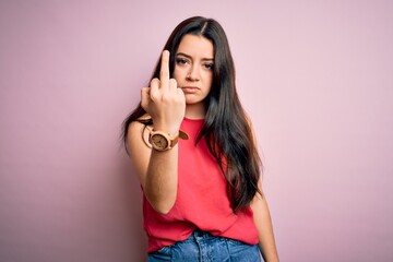 Young brunette woman wearing casual summer shirt over pink isolated background Showing middle finger, impolite and rude fuck off expression - obrazy, fototapety, plakaty