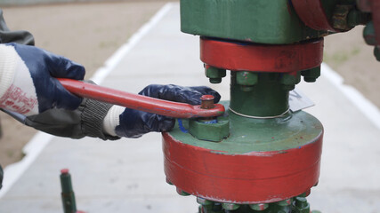 Close up shot of male hands in protective rubber gloves closing valve of wellhead to shut off well....