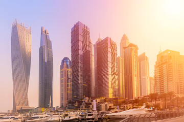 Dubai Marina bay district with ships and skyscrapers at sunset in United Arab Emirates.