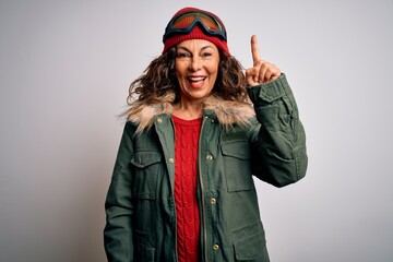 Middle age skier woman wearing snow sportswear and ski goggles over white background pointing finger up with successful idea. Exited and happy. Number one.
