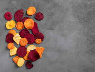 healthy organic vegetable chips from beets, turnips and carrots on a dark concrete background....