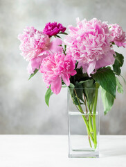 colorful bouquet of assorted peonies in a square glass vase on a white table. Cozy home concept. vertical image. place for text