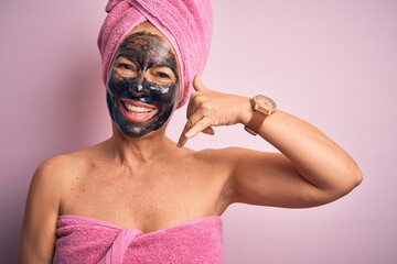 Middle age brunette woman wearing beauty black face mask over isolated pink background smiling doing phone gesture with hand and fingers like talking on the telephone. Communicating concepts.