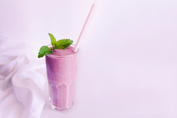 Transparent tall faceted glass with strawberry-blueberry smoothie on a delicate pink background