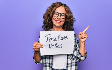 Middle age woman asking for optimistic attitude holding paper with positive vibes message smiling...