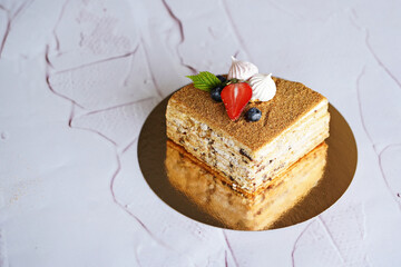layered honey cake in a cut on a gold stand on a white background decorated with white marshmallows and fresh berries