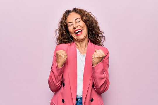 Middle age beautiful businesswoman wearing jacket standing over isolated pink background celebrating surprised and amazed for success with arms raised and eyes closed