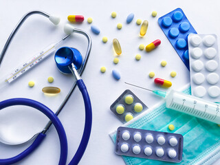 medical supplies doctor, funds for the treatment of the patient - the stethoscope, protective mask, pills, thermometer, syringe on the background of a white textured rough sheet