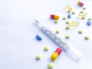 A lot of colorful pills and thermometer - on the right, against a white textured rough sheet of paper with space for text