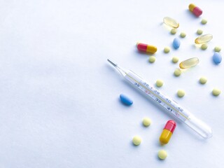 A lot of colorful pills and thermometer - on the right, against a white textured rough sheet of paper with space for text