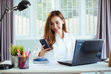 happy young cheerful businesswoman at home office working on smartphone and laptop