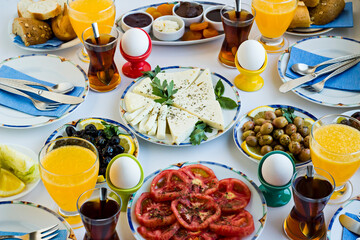 Elegant European or German Breakfast with sliced of tomato,cucumber,cheese,olives,fresh orange juice,tea and boiled eggs designed four service on white table.