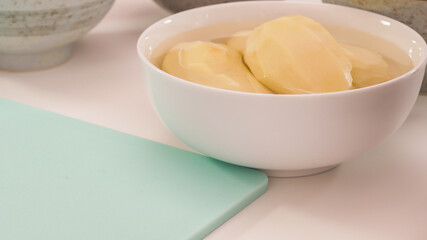 Peeled potato in a bowl close up on white kitchen table