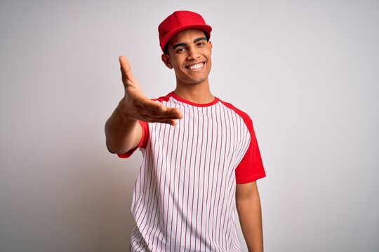 Young handsome african american sportsman wearing striped baseball t-shirt and cap smiling cheerful offering palm hand giving assistance and acceptance.