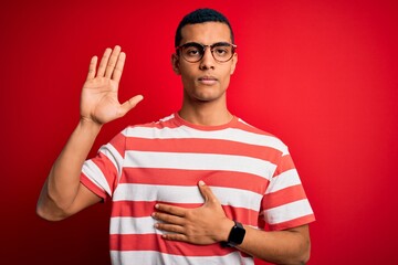 Young handsome african american man wearing casual striped t-shirt and glasses Swearing with hand on chest and open palm, making a loyalty promise oath