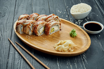 Classic japanese sushi rolls - philadelphia rolls with cream cheese, cucumber, avocado and eel on a bamboo plate on a black wooden background