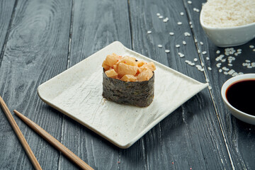Classic japanese sushi rolls - gunkan with scallop and spicy white sauce on a white ceramic plate on a black wooden background. Close up