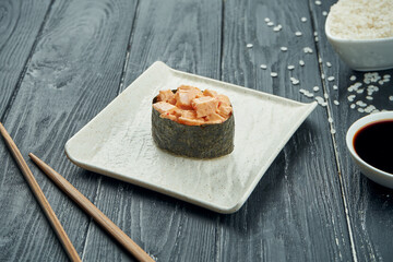 Classic japanese sushi rolls - gunkan with chicken and spicy white sauce on a white ceramic plate on a black wooden background. Close up