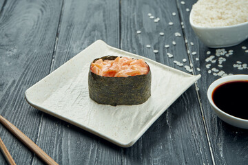 Classic japanese sushi rolls - gunkan with salmon and spicy white sauce on a white ceramic plate on a black wooden background. Close up