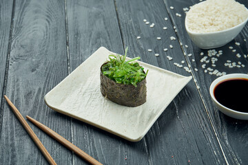 Classic japanese sushi rolls - gunkan with Hiashi Wakame and spicy white sauce on a white ceramic plate on a black wooden background. Close up