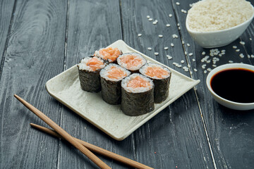 Classic japanese sushi rolls - maki rolls with salmon on a white, ceramic plate on a black wooden background